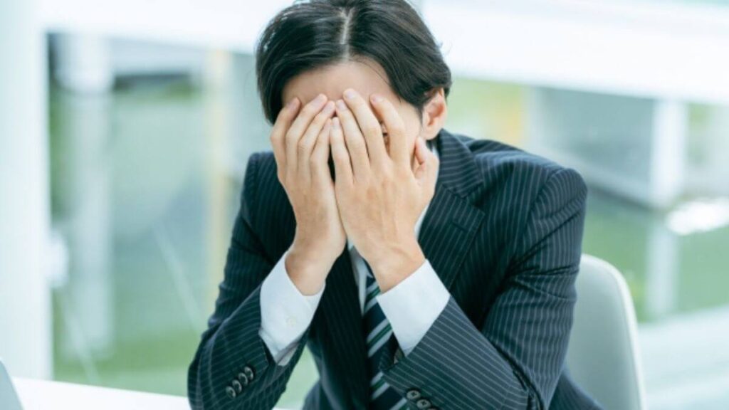 顔を両手で覆うスーツ姿の男性