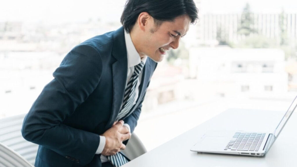 席で胃痛に耐えるスーツ姿の若い男性