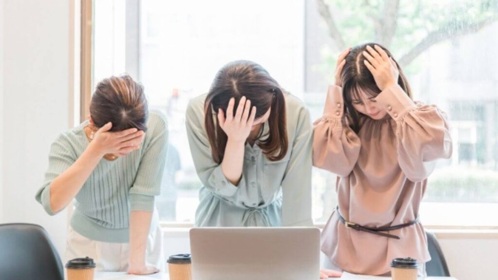 机の前で頭を抱える若い女性3人