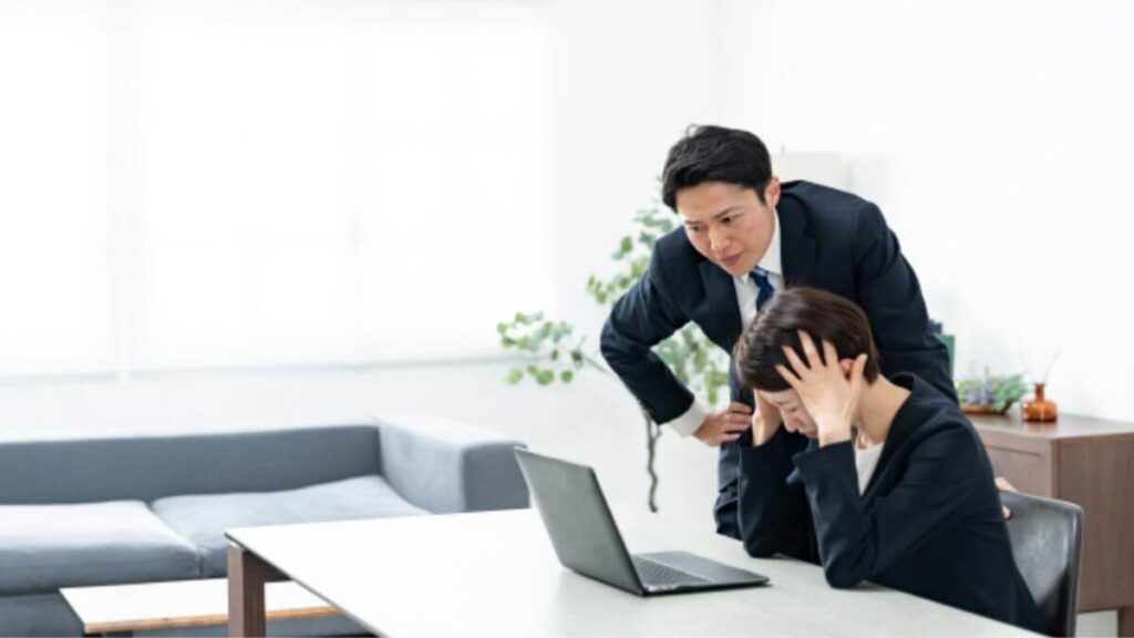 困った顔をしながら仕事をするスーツ姿の男女