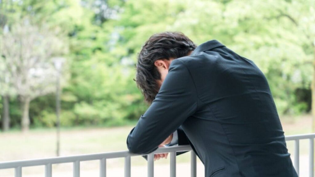 ベランダで落ち込むスーツ姿の若い男性